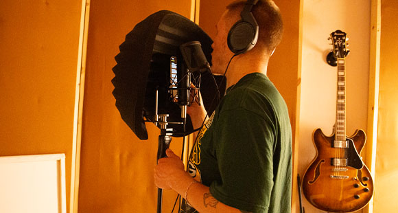 a man recording a song with a guitar on the wall in the background