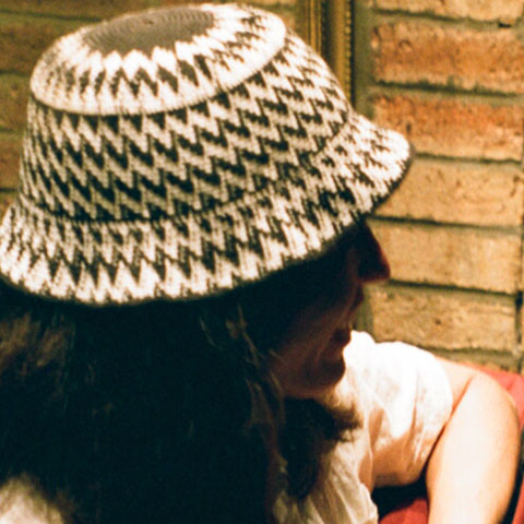 a smiling lady wearing a hat, sitting on a sofa in a brick room