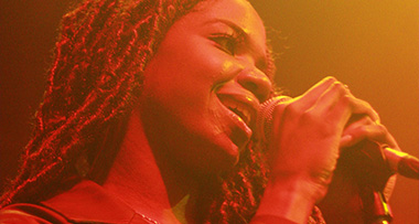 a woman singing into a microphone in an orange-lit room